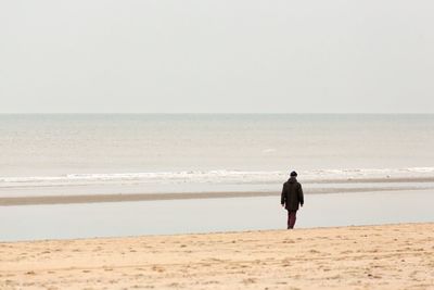 Rear view of woman walking on beach against clear sky