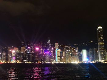 Illuminated buildings by river against sky at night