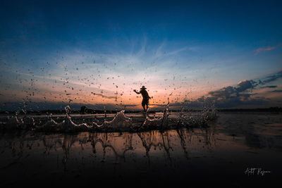 Silhouette man by sea against sky during sunset