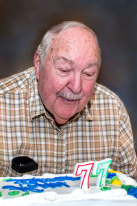 A senior man blows out the candles on his cake for his 77th birthday