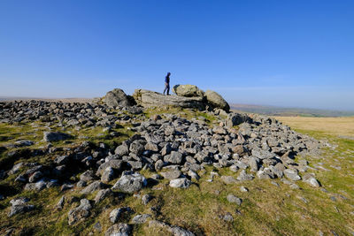 Man standing on rock against clear blue sky