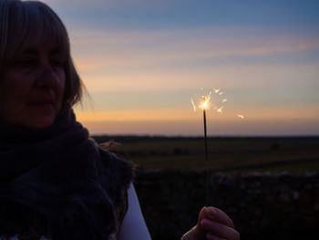 Portrait of woman holding dandelion on field against sky during sunset