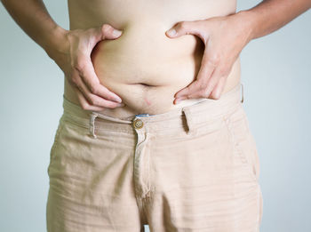 Midsection of man holding belly against gray background