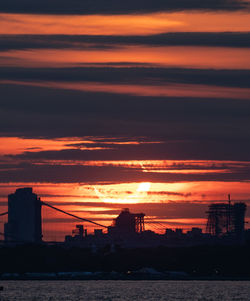 Silhouette city by sea against romantic sky at sunset