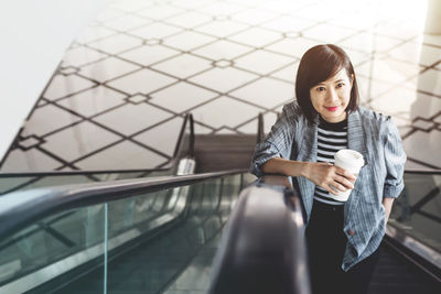 High angle view of smiling mature woman standing on escalator