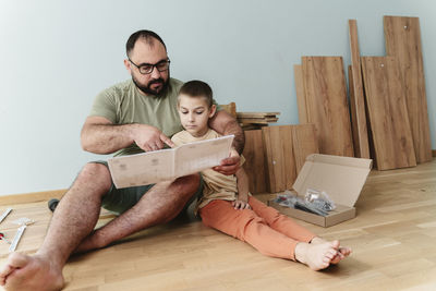 Man with son reading instruction manual sitting on floor at home