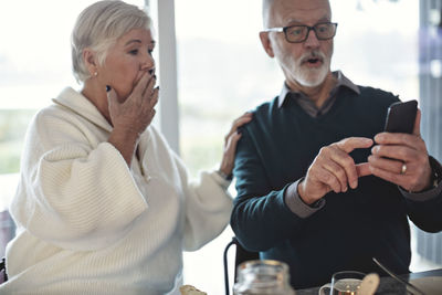 Shocked senior couple using smart phone while sitting in living room