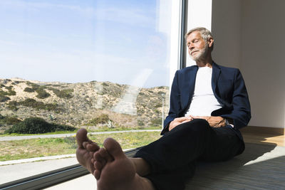 Senior businessman sitting at panorama window with closed eyes