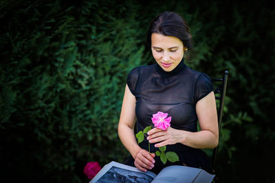 Young woman sitting in a garden with a big book and a rose flower
