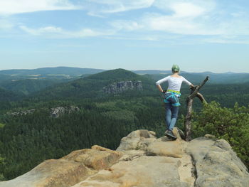 Rear view of teenage girl standing on cliff against sky