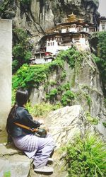 Rear view of woman sitting on rock at taktsang monastery