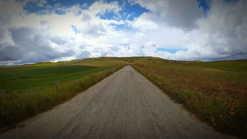 Empty road amidst field against sky