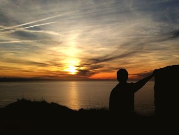 Silhouette man standing by sea against sky during sunset