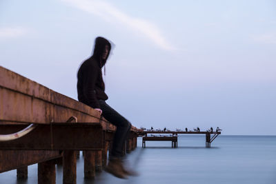 Side view of man sitting on pier over sea during winter