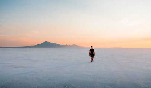 Rear view of man standing in sea against sky during sunset