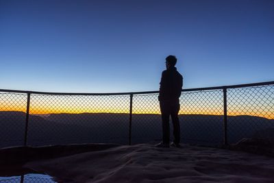 Silhouette man standing at observation point against clear blue sky at morning