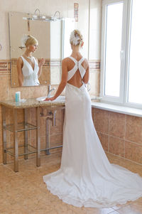 Rear view of bride looking away while standing in front of mirror
