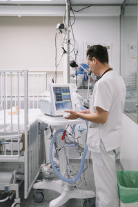 Back view of unrecognizable doctor male adjusting and controlling parameters medical device in clinic