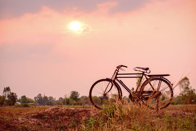 Bicycle on field against sky during sunset
