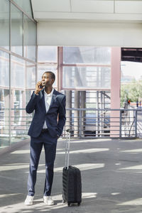 Young businessman with suitcase talking on smart phone at railroad station