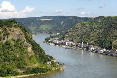 The river rhine in western germany flows between the hills covered with forest, visible buildings.