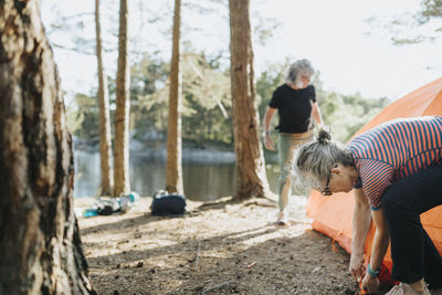 Two senior women setting up tent at campsite at lakeshore