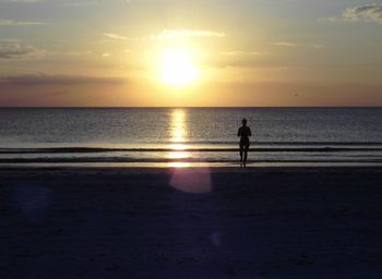 Silhouette woman walking at beach against sky during sunset