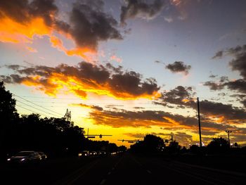 Cars on road against dramatic sky during sunset