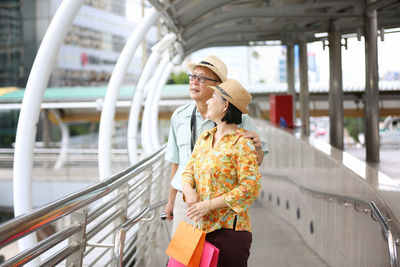 Smiling couple holding shopping bags while standing at covered bridge