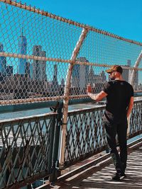 Rear view of man standing by railing against sky