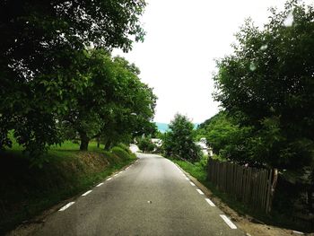 Empty road amidst trees against sky in city