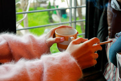 Cropped image of woman holding cigarette and coffee cup