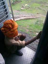 Man wearing orange turban while crouching on train doorway