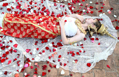 Woman in traditional clothing lying on petals over textile