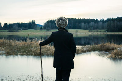 Rear view of man standing by lake against sky
