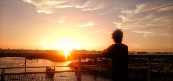 Rear view of silhouette woman standing against sea during sunset