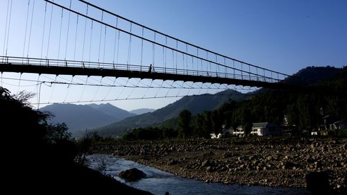 Low angle view of footbridge over river against blue sky