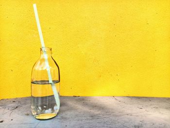 Glass bottle on table against yellow wall