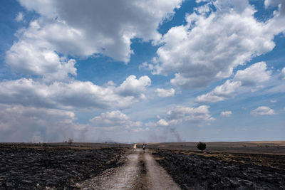 Dirt road amidst field against sky