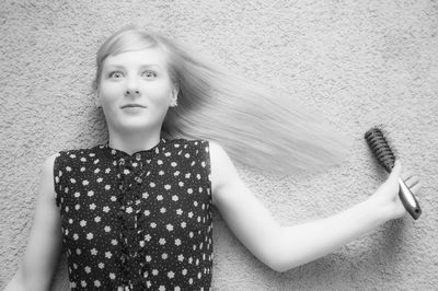 Portrait of young woman holding hairbrush against wall