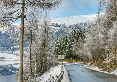 Snow covered road by trees against mountain