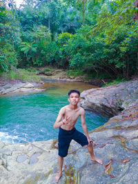 Portrait of shirtless young man on rock in forest