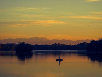 Silhouette trees by calm lake against sky during sunset