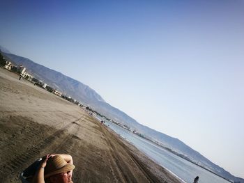 Tilt image of man relaxing at beach against sky