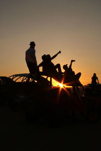 Friends taking selfie while sitting on off-road vehicle against sky during sunset