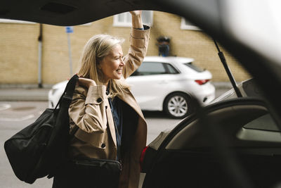 Businesswoman carrying luggage while opening car trunk