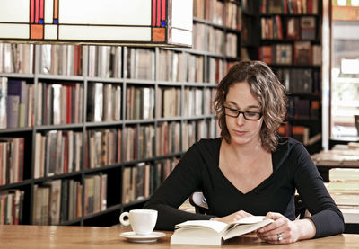 Woman drinking coffee while reading at bookstore