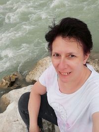 Portrait of smiling man sitting on rock by sea