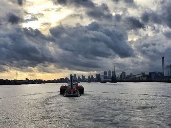 Boat sailing on river in city against sky during sunset