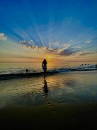 Rear view of woman walking at beach against sky during sunset in the netherlands